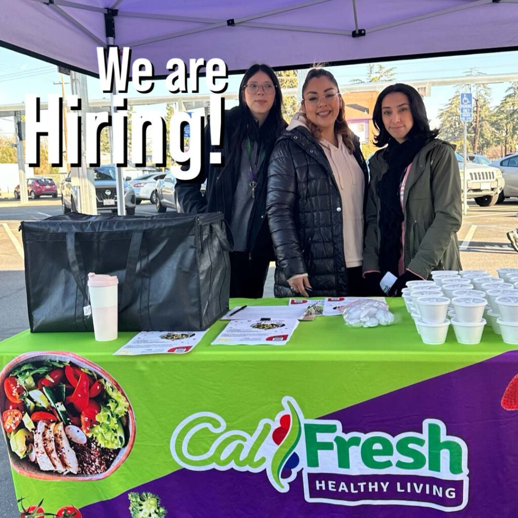 We are hiring! Image of three Catholic Charities employees manning a CalFresh booth.